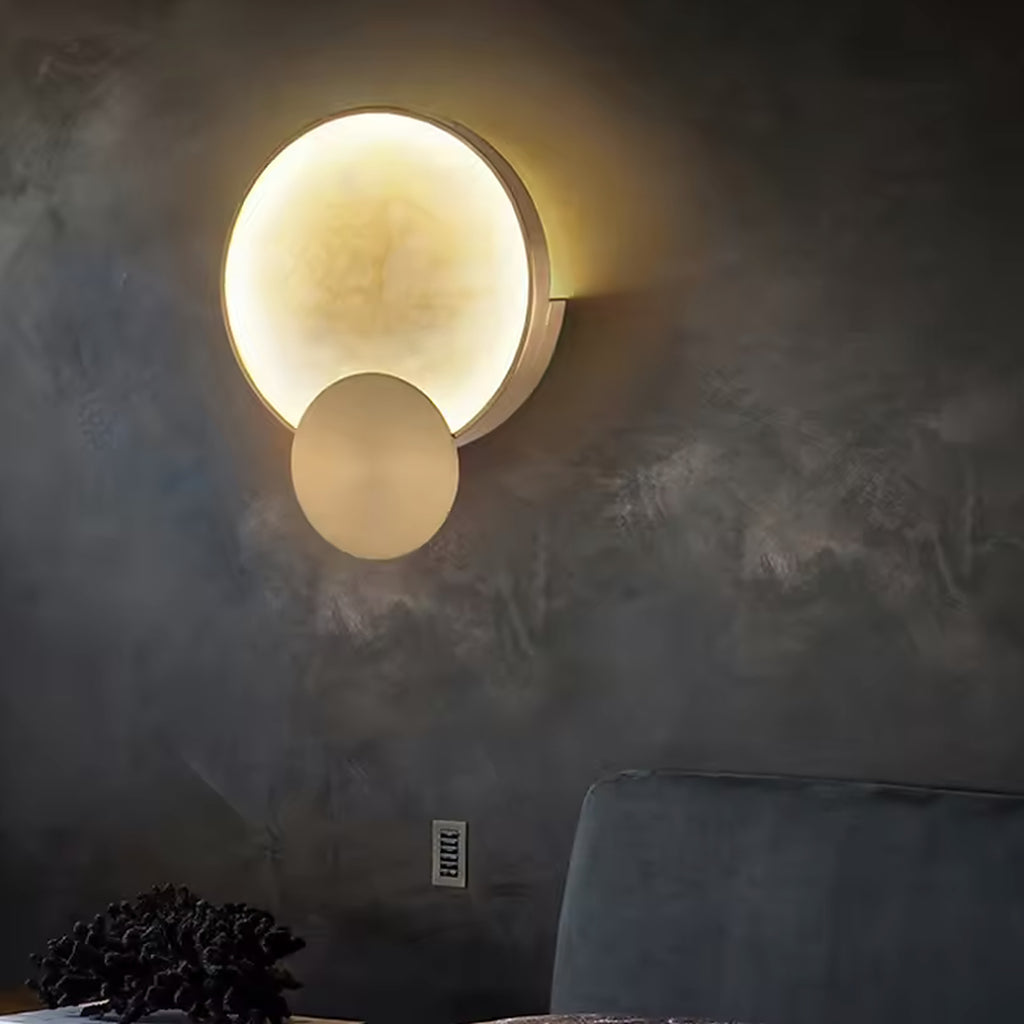 Alabaster and gold wall sconce glowing against a dark plaster wall