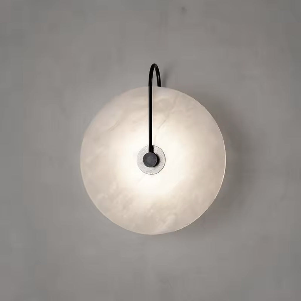 Alabaster disc wall sconce glowing on a plain plaster wall