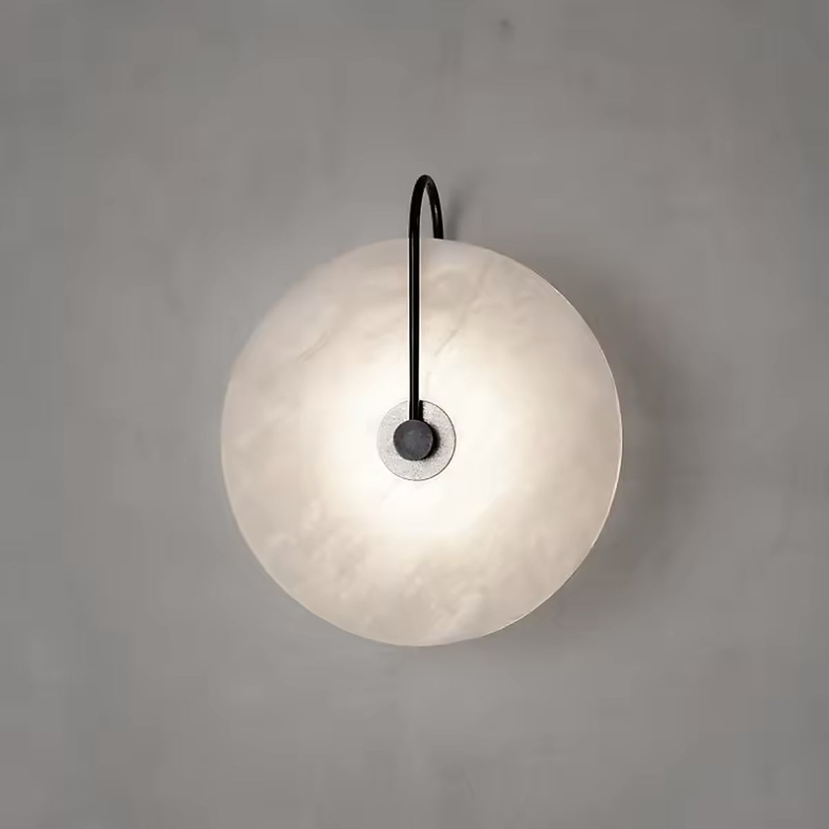 Alabaster disc wall sconce glowing on a plain plaster wall