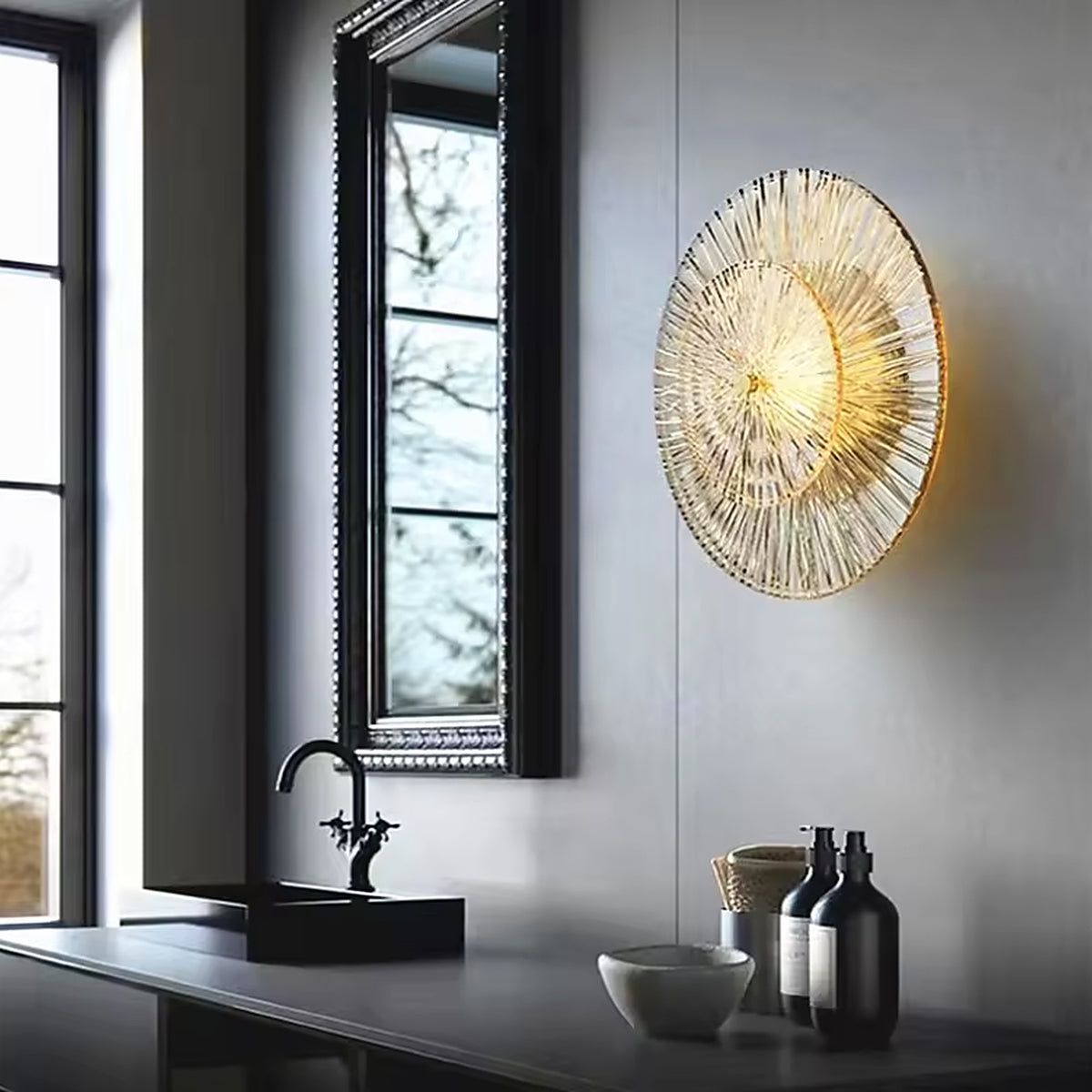 Art deco glass wall sconce on a grey wall beside a black stone counter