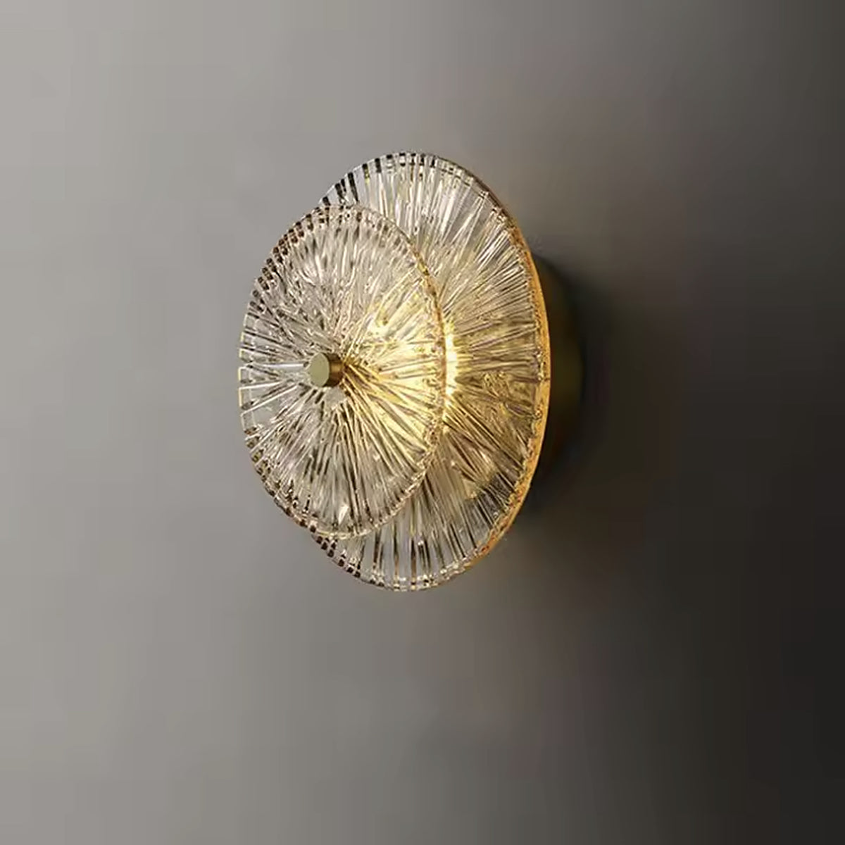 Art deco ribbed glass wall sconce with two offset discs on a gold hub, switched on