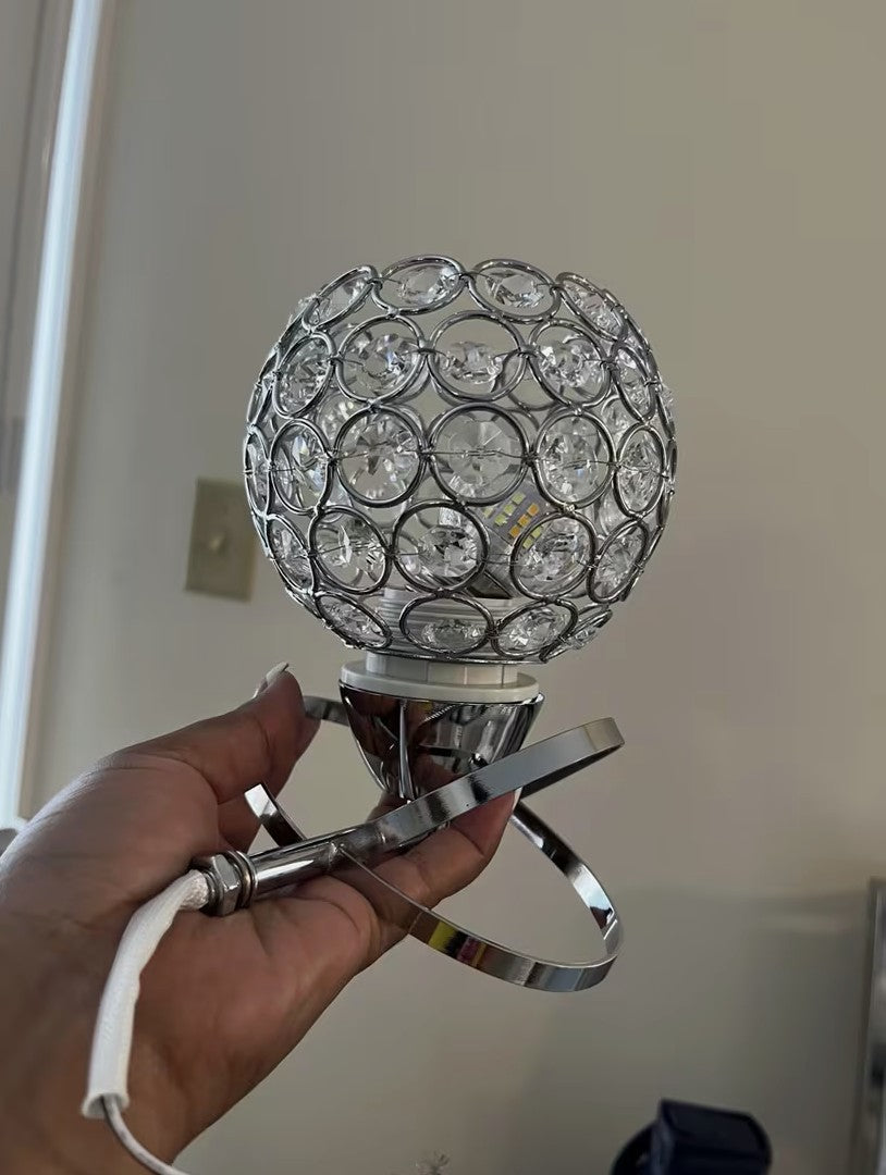 Crystal globe wall sconce held in hand, crossed steel ribbons