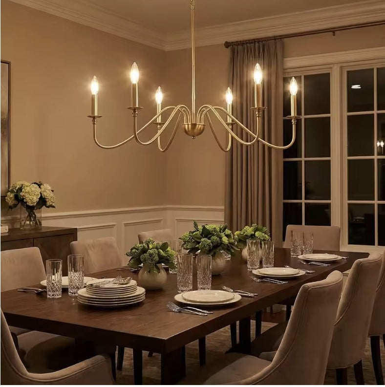 Gold farmhouse candle chandelier lit above a set dining table in the evening