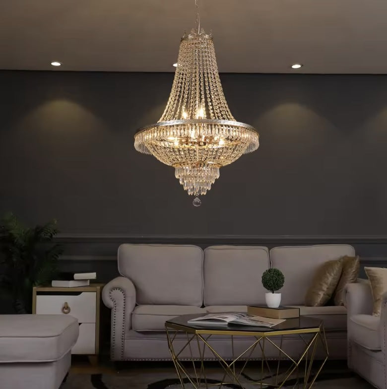 Large empire crystal chandelier in gold lit above a sofa in a grey living room Image