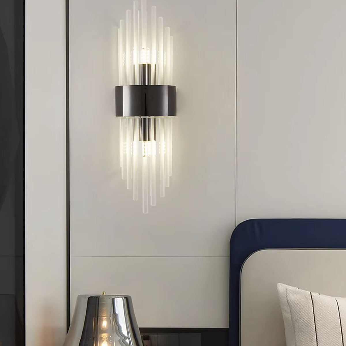 Black linear glass rod wall sconce beside a bed