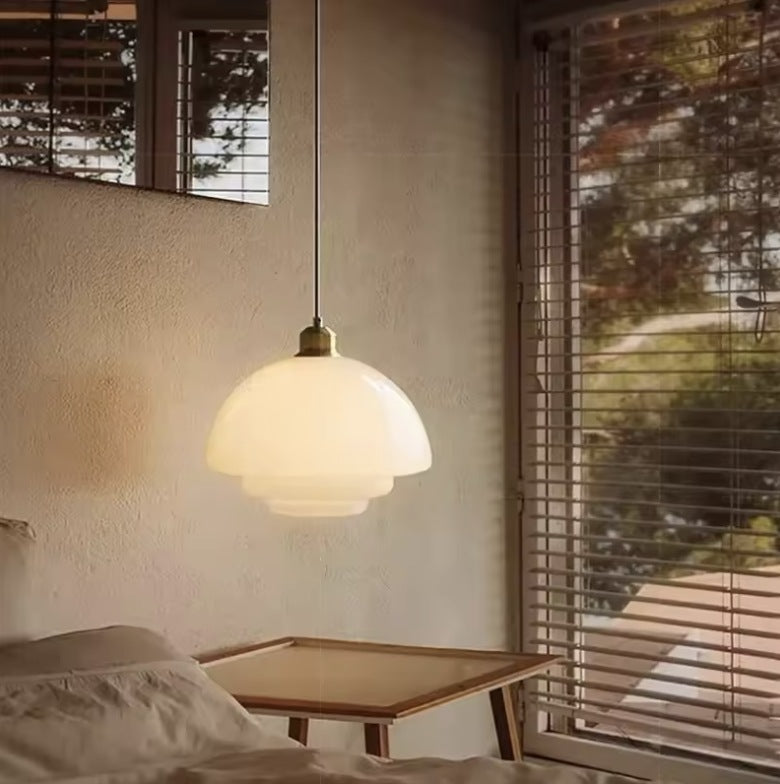 Milk glass pendant light above a bedside table beside a bed, warm evening light