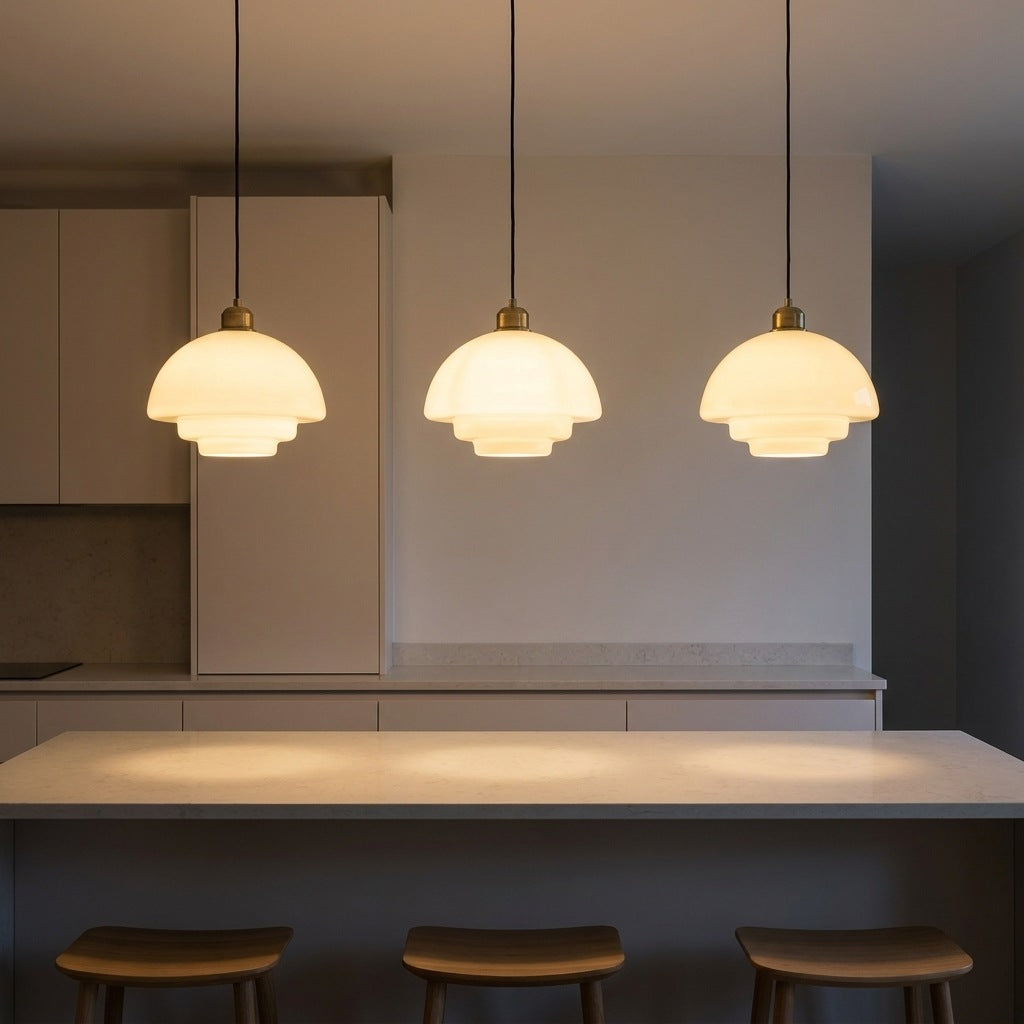 Three milk glass pendant lights in a row above a modern kitchen island, lit