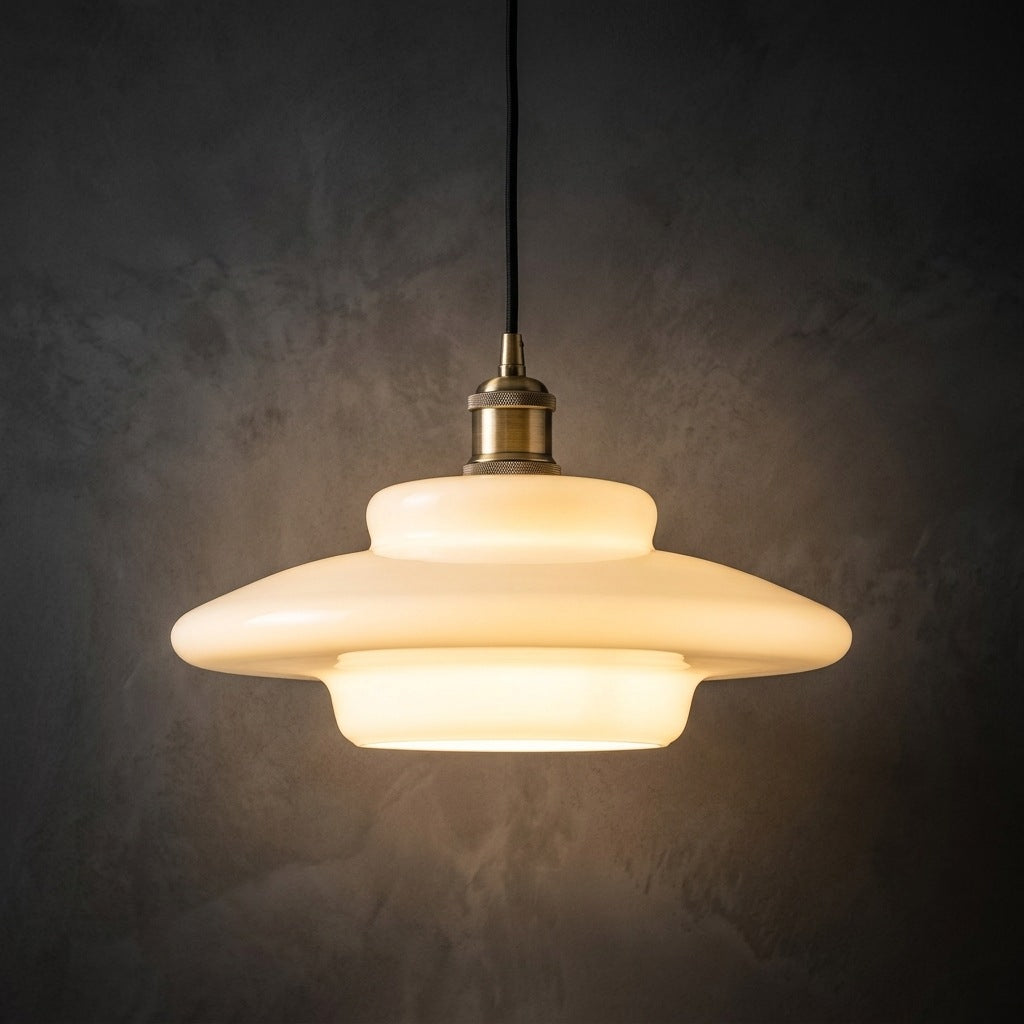 Milk glass pendant light, wide saucer profile, lit against a dark plaster wall