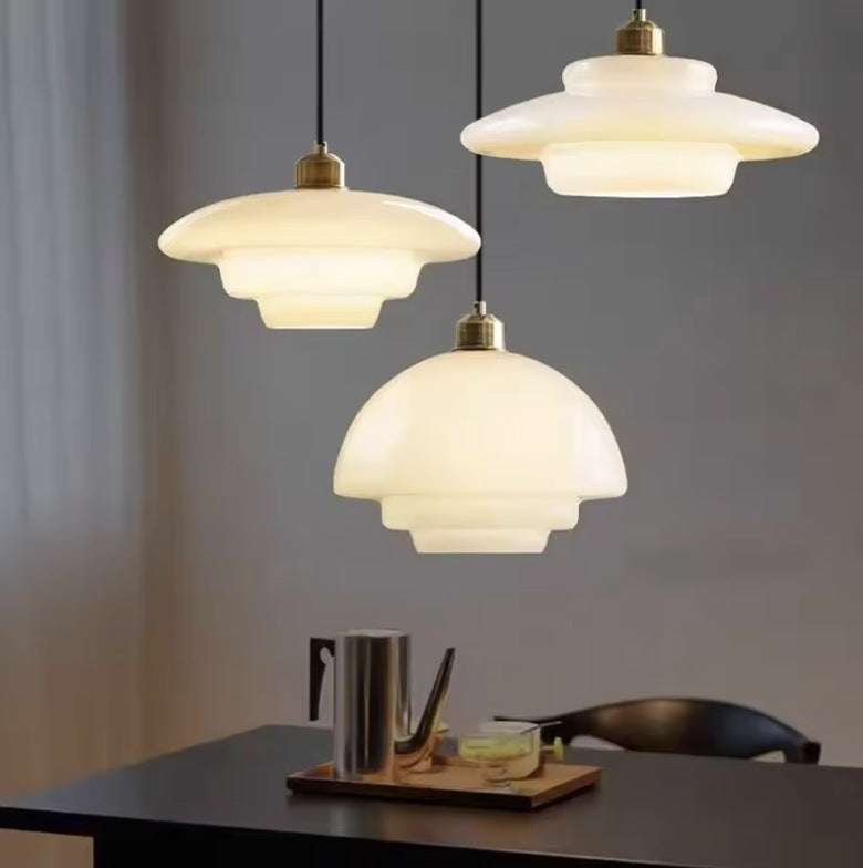 Three milk glass pendant lights hung at different heights over a dark table Image
