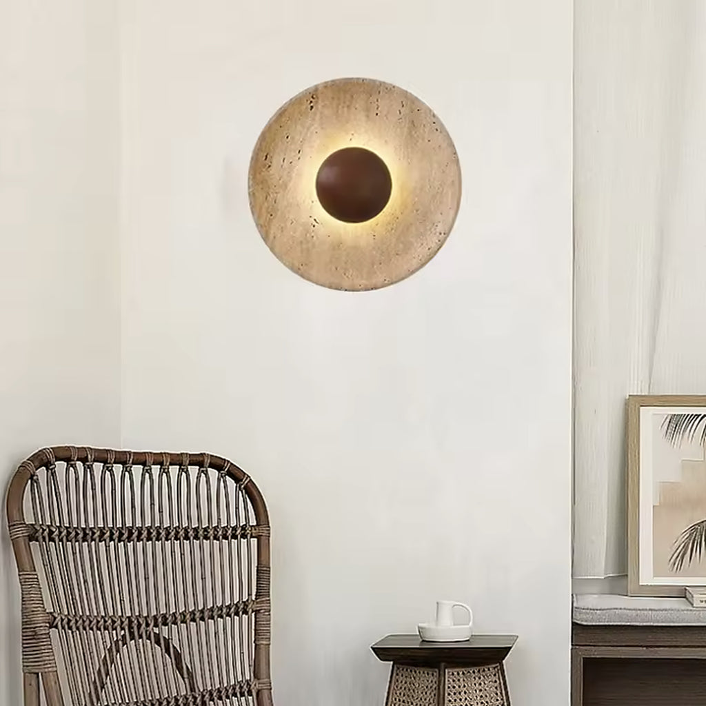 Travertine wall sconce lighting a plain wall above a rattan chair