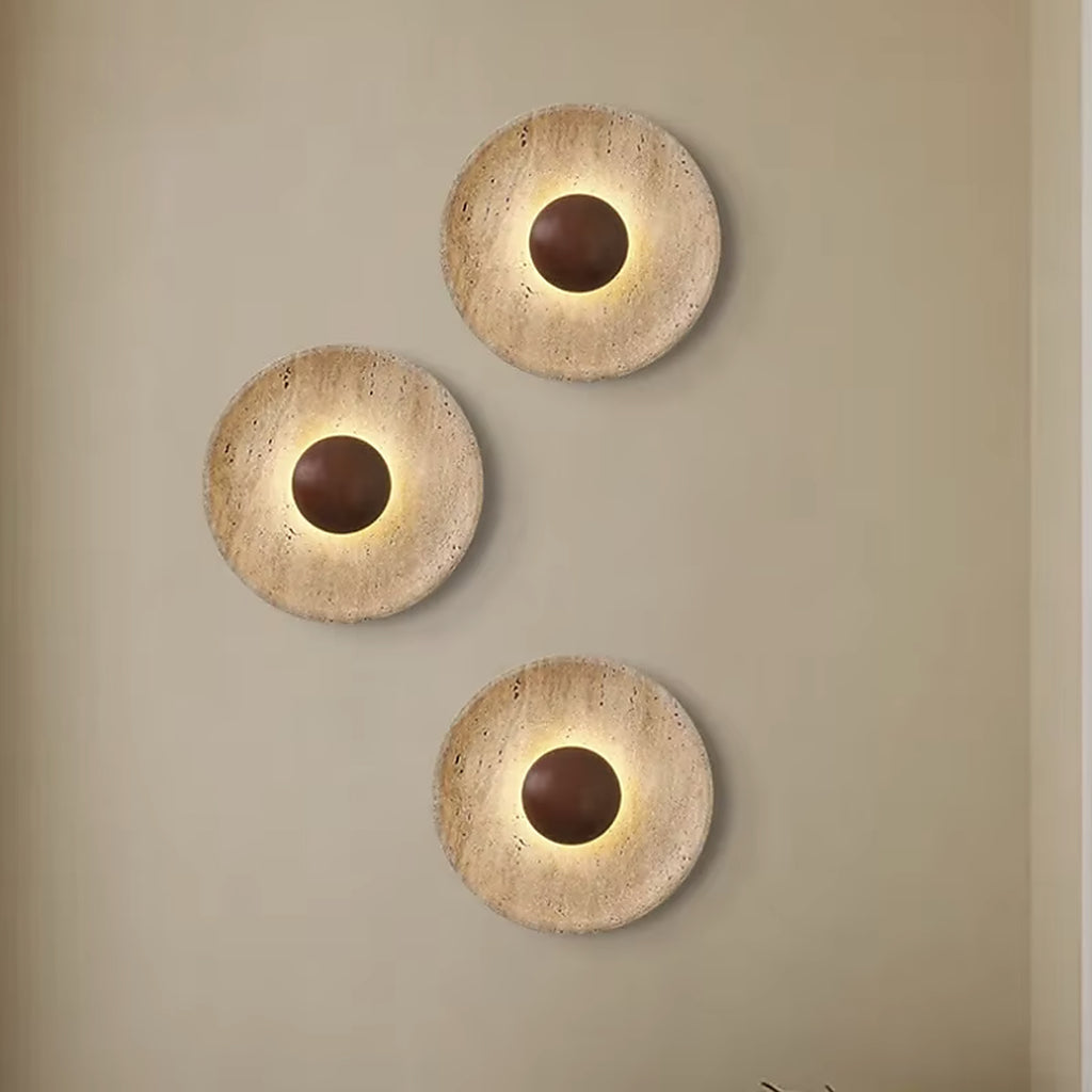 Three travertine wall sconces staggered on a warm beige wall