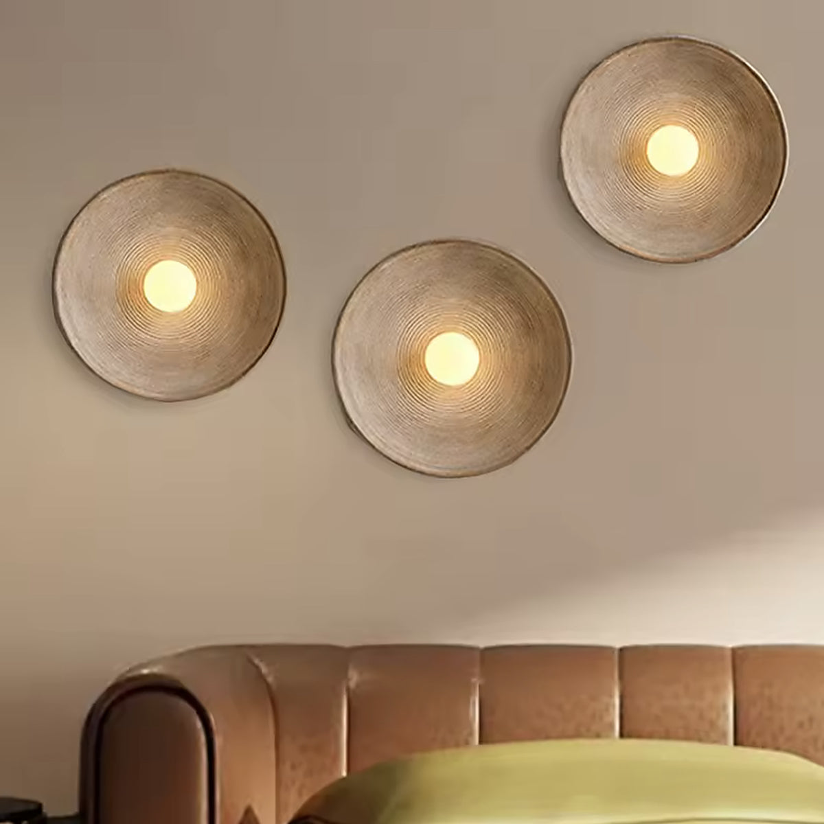 Three nordic round wall sconces staggered above a leather bed