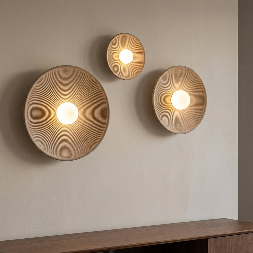 Three nordic round wall sconces in three different diameters arranged on a plaster wall