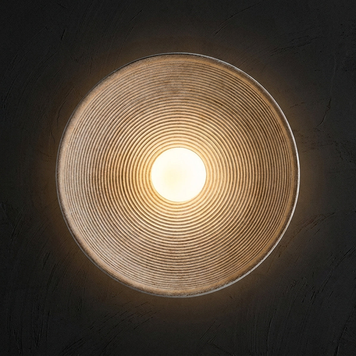 Nordic round wall sconce with concentric ribbing and an opal globe, switched on against a black plaster wall