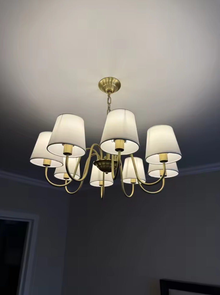 Vintage brass chandelier with eight fabric shades lit beside a window