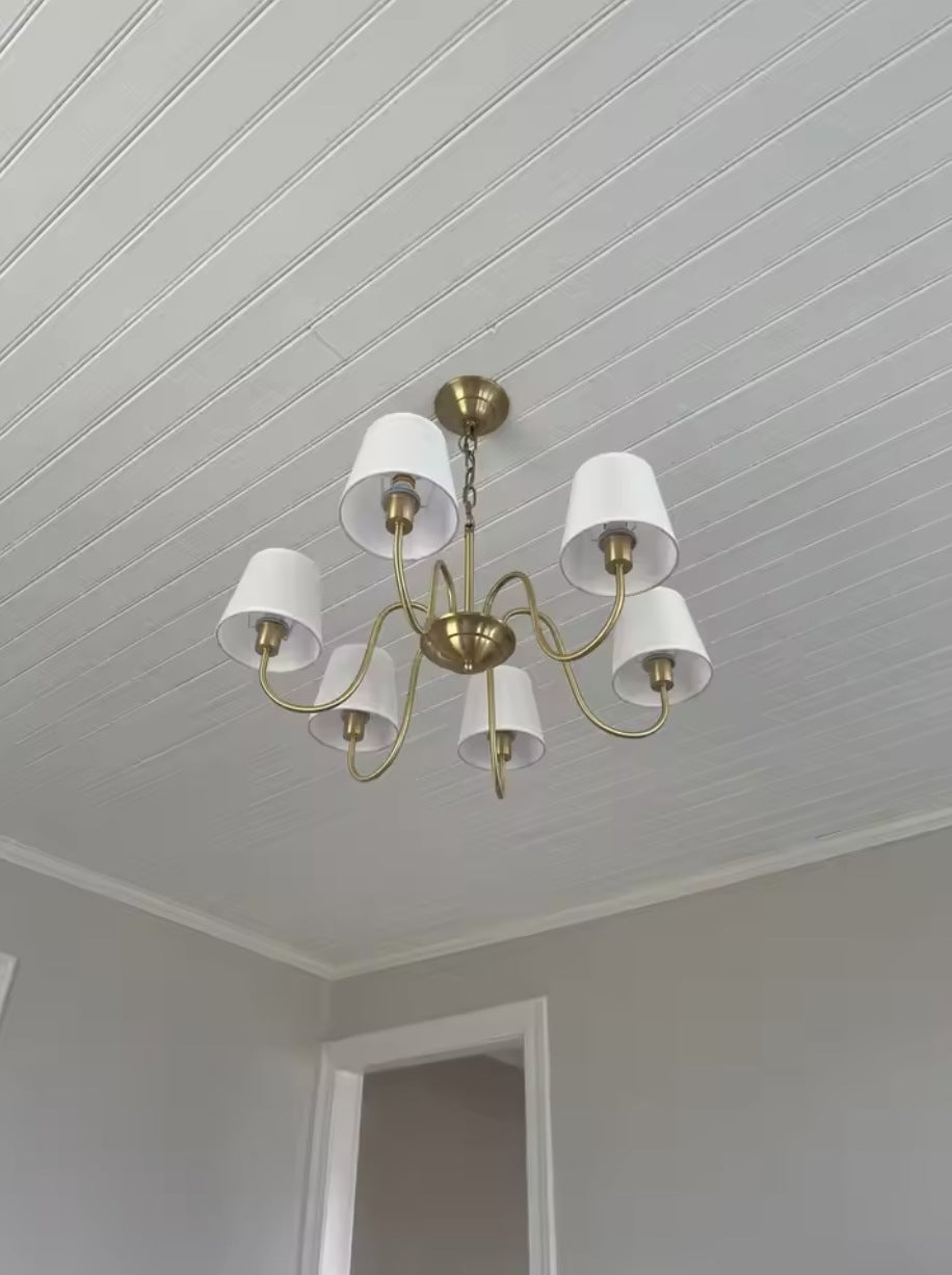 Vintage brass chandelier with eight fabric shades lit in a grey room